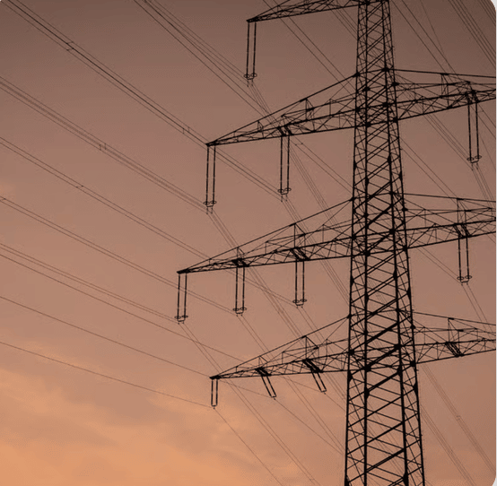 A high-voltage transmission tower and power lines silhouetted against a hazy orange sky.